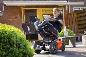 A-woman-in-a-power-wheelchair-using-tilting-and-lifting-funtion-reading-newspaper-outdoor-under-the-sunlight