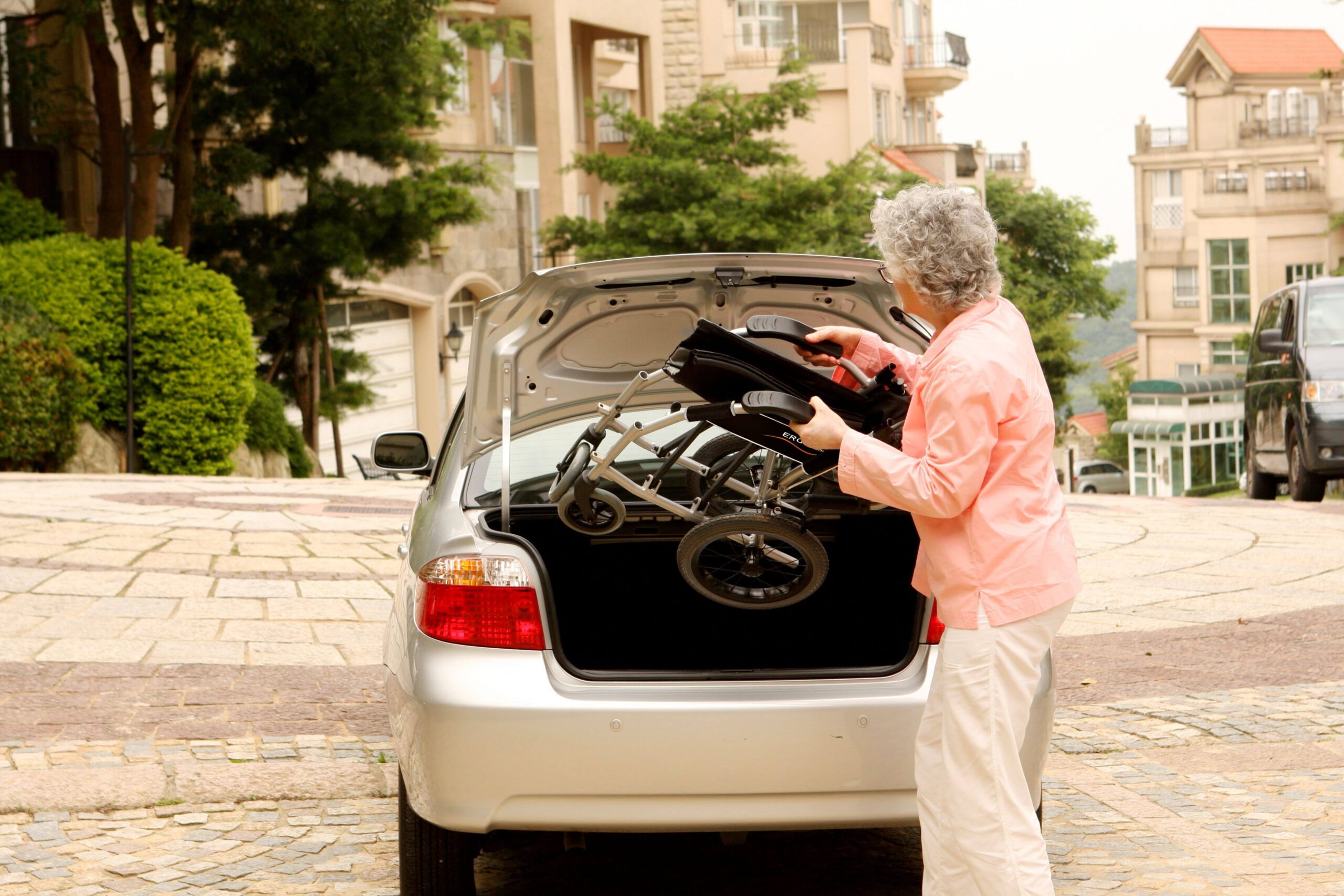 the lady puts a folding wheelchair into the trunk of a car 