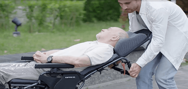 person helping an elderly user recline in the wheelchair